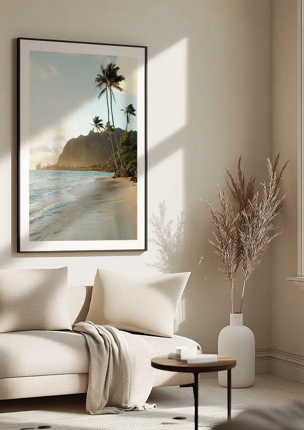 Een minimalistische woonkamer is voorzien van een groot ingelijst Strand Bij zonsondergang Schilderij van CollageDepot van een strandtafereel met palmbomen en bergen. Het meubilair in neutrale tinten bestaat uit een lichtgekleurde bank met een deken en een kleine ronde tafel. Op de vloer wordt een vaas met gedroogde planten geplaatst, als aanvulling op de serene wanddecoratie.,Zwart