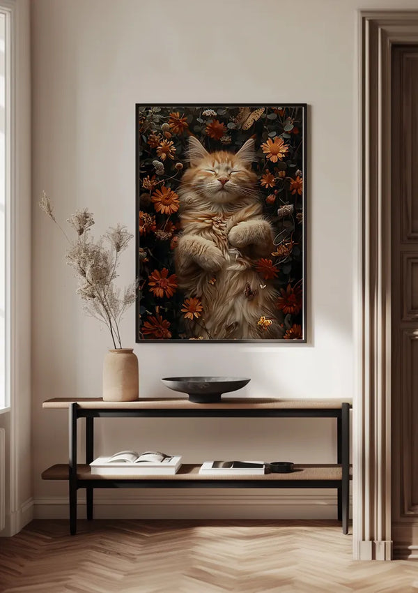 Een ingelijste foto van een relaxte, donzige oranje kat omringd door bloemen (Cat Nap Between Beautiful Flowers Schilderij van CollageDepot) hangt aan een lichtgekleurde muur boven een minimalistische houten consoletafel. Op de tafel staat een bruine vaas met gedroogde bloemen, een lege ondiepe schaal en een open boek, alles geplaatst op een visgraathouten vloer met een magnetisch ophangsysteem.,Zwart
