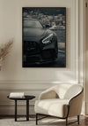 Een **Matzwarte Mercedes AMG GTR Schilderij** van **CollageDepot** hangt aan een witte muur boven een moderne gebogen witte stoel. Naast de stoel staat een klein zwart bijzettafeltje en links is gedeeltelijk een decoratief beige pampasgras-arrangement zichtbaar. Deze stijlvolle wanddecoratie maakt gebruik van een magnetisch ophangsysteem voor eenvoudige weergave.,Zwart