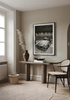 Een minimalistische woonkamerhoek met beige muren is voorzien van een ingelijste foto van een klassiek Mercedes SL300-schilderij van CollageDepot boven een rustieke houten consoletafel. Op de tafel staat een hoge vaas met pampasgras en een kom. Een geweven mand en een rieten stoel staan vlakbij, wat bijdraagt aan de gezellige wanddecoratie.,Zwart