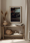 Een minimalistische kamer heeft een ingelijste foto van een zwarte Porsche GT3 In Een Garage van CollageDepot aan de muur. Onder de foto staat op een houten consoletafel een grote keramische vaas, een kom, een sierpot en kleine kunstwerken. Neutrale tinten domineren het decor, met zachte verlichting en gordijnen.,Lichtbruin