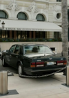 Een klassiek zwart CollageDepot aaa 001 - auto geparkeerd buiten het chique Louis XV-restaurant Alain Ducasse, met de gevel zichtbaar op de achtergrond, en de auto aan de achterkant vastgeketend aan een paal.-