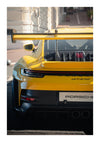 Achteraanzicht van een gele CollageDepot aaa 011 - auto geparkeerd in een stadsstraat, met een prominente achtervleugel en gecentreerde dubbele uitlaten. Het licht baadt in de gestroomlijnde sportwagen en benadrukt de designdetails.-
