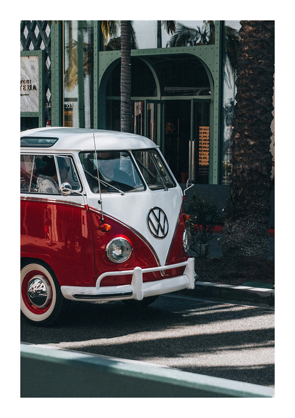 Een rood-wit vintage Volkswagen-busje van CollageDepot geparkeerd in een zonnige straat vol palmbomen en een gebouw met gebogen deuropeningen op de achtergrond.-