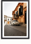 Een CollageDepot Witte Vintage Fiat 500 Schilderij staat geparkeerd in een rustige straat vol oude gebouwen met een mix van lichte en donkere luiken. Het tafereel, perfect voor wanddecoratie, is vastgelegd in een verticaal kader en roept een gevoel van nostalgie op in een stedelijke omgeving.,Zwart-Met,Lichtbruin-Met,showOne,Met