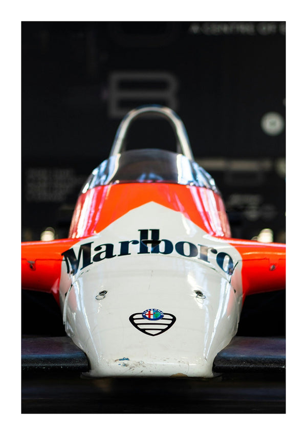Vooraanzicht van een vintage racewagen Formule 1-auto. De auto heeft een opvallend rood-wit kleurenschema, waarbij het Marlboro-logo prominent op de neus is weergegeven. Met een gedeeltelijk zichtbare cockpit lijkt dit opvallende stuk op een Alfa Romeo 'Marlboro'-schilderij van CollageDepot, dat binnenshuis stil lijkt te staan alsof het is opgehangen aan een onzichtbaar magnetisch ophangsysteem.