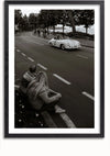 Zwart-witfoto van een klassieke auto die over een weg rijdt, omzoomd met bomen en toeschouwers. Op de voorgrond zitten twee mensen met lang haar in truien op een stoeprand te kijken naar de voorbijrijdende auto. Deze afbeelding zou een prachtige wanddecoratie kunnen zijn, nog extra versterkt door gebruik te maken van een magnetisch ophangsysteem. Weergegeven als Racende Porsche 356 Schilderij van CollageDepot, zou het de aandacht trekken en elegantie toevoegen aan elke ruimte.