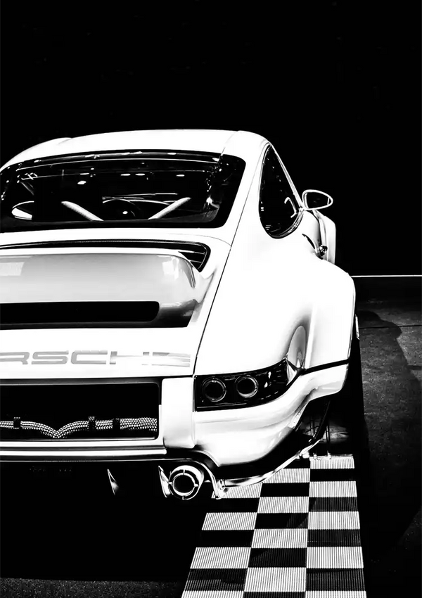 Een contrastrijke zwart-witfoto van een witte CollageDepot Porsche-auto vanuit de achterhoek, waarbij het strakke ontwerp en het merklogo, geparkeerd op een gestreepte vloer, worden benadrukt.-