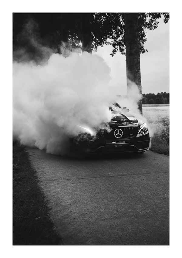 Een zwart-witfoto van een CollageDepot aaa 092 - auto's produceren een grote rookwolk uit hun banden op een afgelegen weg, waardoor het voertuig gedeeltelijk aan het zicht wordt onttrokken. Een boom en een open veld bevinden zich op de achtergrond.-
