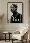 Aan de muur hangt een ingelijste zwart-witfoto van een man met gevlochten haar en een ronde bril, die dient als prachtige wanddecoratie. De proefpersoon draagt een pak en het woord 'Dior' is prominent zichtbaar. Voor de foto staat een lichtgekleurde moderne fauteuil en een kleine ronde tafel. Deze elegante scène toont het "Stijlvolle Man Schilderij" van CollageDepot.,Zwart