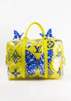 Een groot, geel CollageDepot Louis Vuitton Gele Handtas Schilderij met blauwe vlindermotieven, waaronder het LV-logo en bloempatronen. De tas heeft gele handvatten, een doorzichtige plastic omhulling met extra blauwe vlinderaccenten en lijkt op een stijlvolle gele reistas, perfect voor elke reiziger.