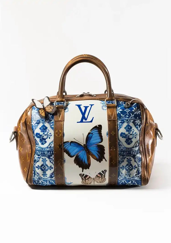 Een CollageDepot Louis Vuitton Bruine Handtas Schilderij met een bruin leren handvat en accenten. De tas heeft blauwe bloemenpatronen, een opvallende blauwe vlinder en de initialen "LV" op een witte achtergrond. Perfect als accessoire en als wanddecoratie, met een vlinderdetail op een van de handgrepen.
