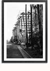 Een zwart-witfoto toont een straatbeeld met hoge palmbomen langs het trottoir. Er is een rij geparkeerde auto's zichtbaar en op de achtergrond is een gebouw te zien met een groot bord en een bord met een maximumsnelheid van 40 km/uur, perfect vastgelegd voor wanddecoratie met behulp van een magnetisch ophangsysteem met het schilderij Rodeo Drive Los Angeles van CollageDepot.