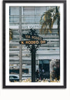 Een straatnaambord op de hoek van Via Rodeo en N. Rodeo Dr. staat op de voorgrond, met een Louis Vuitton-winkel en palmbomen op de achtergrond. Deze elegante foto, perfect als wanddecoratie, is omlijst met een zwarte rand en beschikt over een magnetisch ophangsysteem voor eenvoudige weergave. Het Wegwijzer Louis Vuitton Winkel Schilderij van CollageDepot belichaamt verfijning en stijl.,Zwart-Met,Lichtbruin-Met,showOne,Met
