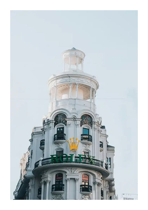 Een wit gebouw met meerdere verdiepingen, ronde architectuur en ingewikkelde details. Er staat een groen bord met het woord "ROLEX" en een gouden kroonlogo eronder. De bovenkant van het gebouw heeft een cirkelvormige torenachtige structuur, die doet denken aan een schilderij van Rolex Store Madrid van CollageDepot tegen de heldere lucht op de achtergrond.
