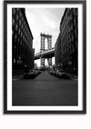 Een zwart-wit schilderij van de Manhattan Bridge in New York City, elegant ingelijst, toont de brug gecentreerd tussen twee hoge gebouwen met geparkeerde auto's langs de straat. Het perspectief vanuit een geplaveide straat voegt een vleugje nostalgie toe aan dit opvallende Manhattan Bridge Schilderij van CollageDepot.,Zwart-Met,Lichtbruin-Met,showOne,Met