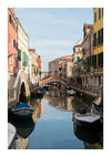 Een smal kanaal in Venetië, Italië, geflankeerd door kleurrijke gebouwen aan beide zijden. Langs de randen van het kanaal liggen verschillende boten afgemeerd. Een sierlijke stenen brug overspant in de verte het water, onder een helderblauwe lucht. Dit tafereel wordt vastgelegd als een CollageDepot Serene Gracht In Venetië Schilderij, een perfecte wanddecoratie voor elke kamer.-