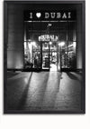 Een zwart-witfoto toont een winkel met een bord met de tekst "I ♥ DUBAI" boven de ingang. De glazen deuren van de winkel worden van binnenuit verlicht en tonen verschillende koopwaar, waaronder I love Dubai-schilderijstukken van CollageDepot. Schaduwen van de verlichting strekken zich uit tot op de stenen stoep voor de winkel.
