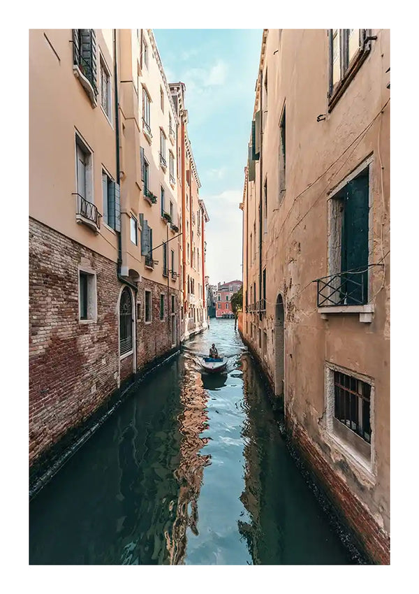 Een smal kanaal in Venetië, Italië, geflankeerd door hoge, verweerde gebouwen. Onder een strakblauwe hemel glijdt een bootje met een persoon aan boord door het kanaal. Het water weerspiegelt de omliggende gebouwen en de boot, waardoor een scène ontstaat die doet denken aan een voortreffelijk Schilderij van Kanaal Venetië van CollageDepot – ideaal voor elke wanddecoratie.-