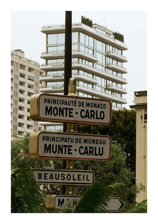 Straatnaamborden in Monaco met "Monte-Carlo" geschreven in het Frans en Monegaskisch (Munte-Carlo), naast een bord dat richting Beausoleil wijst, lijken op een modern schilderij. Op de achtergrond zijn moderne gebouwen met groen te zien, een perfect decor voor wanddecoratie of gebruik met een CollageDepot Monte Carlo bord schilderij magnetisch ophangsysteem.