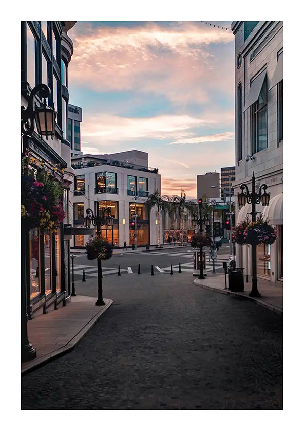 Een rustige stadsstraat in de schemering met gebouwen versierd met bloemenhangende manden, lege voetgangerspaden en esthetische straatlantaarns onder een pastelkleurige hemel uit CollageDepot's baa 073 - landen en steden.-