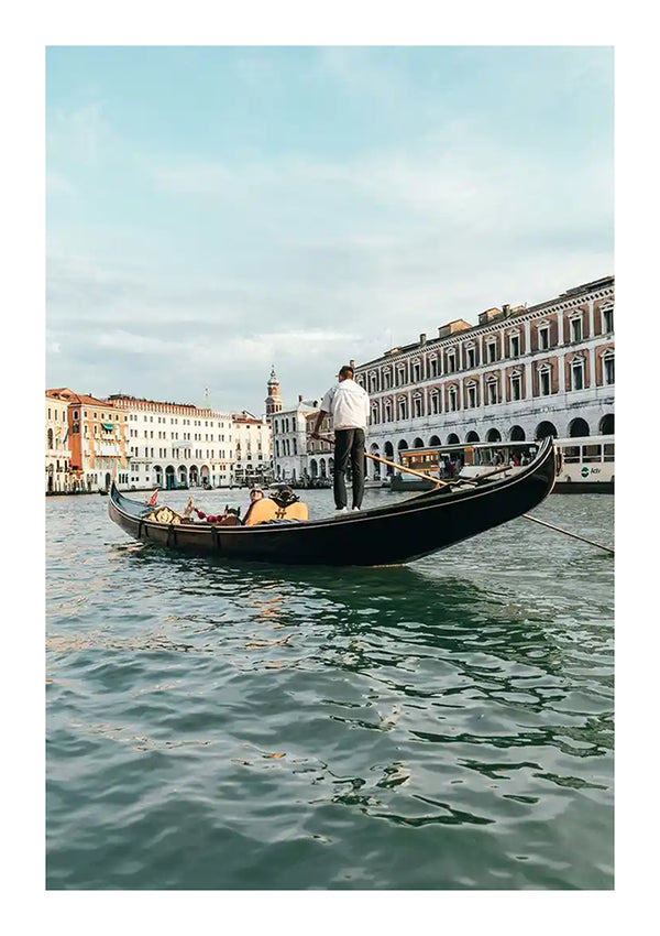 Een gondelier staat en roeit een gondel met passagiers langs een Venetiaans kanaal in Venetië. Historische gebouwen met boogramen en balkons liggen langs de gracht onder een gedeeltelijk bewolkte hemel en lijken op een prachtig schilderij. Het water weerspiegelt de gebouwen en de lucht, waardoor een perfecte wanddecoratie ontstaat, vergelijkbaar met de Gondelier In Een Gondel Schilderij van CollageDepot.-