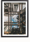 Een CollageDepot bbb 007 - natuurfoto vastgelegd van onder een glazen plafond, omlijst door metalen steunen, met hoge gebouwen en palmbomen tegen een blauwe lucht. In het midden van het beeld is een vliegtuig zichtbaar dat overvliegt. De foto is ingelijst in een zwarte rand.,Zwart-Met,Lichtbruin-Met,showOne,Met