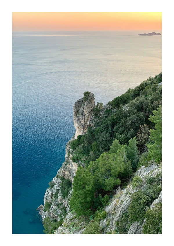 Een schilderachtig uitzicht op een klif aan de kust bij zonsondergang. Dicht groen bedekt de klifwand die naar een kalme blauwe zee leidt, waarbij de horizon een zacht verloop vertoont van roze naar blauw, met de bbb 016 - natuur van CollageDepot.-