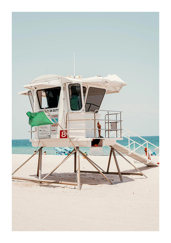 Een strandwachttoren van CollageDepot staat op een zandstrand onder een heldere hemel, met het opschrift "Lifeguard On Duty" met een groene vlag en parasol eraan, met uitzicht op een kalme zee.-