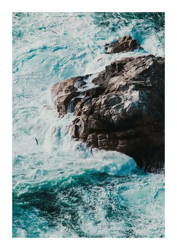 Luchtfoto van turbulente oceaangolven die tegen rotswanden botsen. Het water schuimt en blauw-witte tinten wervelen rond de rotsformaties. Links in het midden van dit Savage Waves Schilderij is een eenzame vogel zichtbaar die boven het water vliegt, waardoor het een prachtige wanddecoratie is met een innovatief ophangsysteem van CollageDepot.-