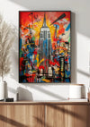 Een ingelijst schilderij van een stadsgezicht met het Empire State Building voor een kleurrijk, abstract Kunstwerk Empire State Building Schilderij van CollageDepot hangt aan een muur. Daaronder versterkt een houten dressoir met potplanten en decoratieve items de wanddecoratie.,Zwart