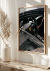 Aan de muur hangt een ingelijst Ferrari Cockpit-schilderij van CollageDepot, met het iconische stuurwiellogo. Daaronder staat een vaas met gedroogde flora sierlijk op een plank, badend in zacht natuurlijk licht. Deze luxe wanddecoratie straalt elegantie en verfijning uit in elke ruimte.,Lichtbruin