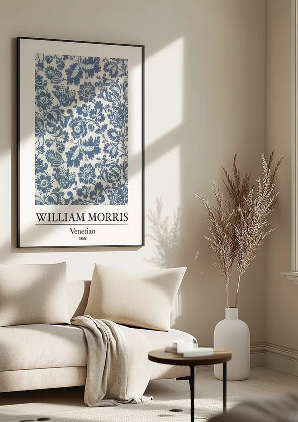 In een woonkamer hangt een ingelijst CollageDepot W. Morris Venetian Schilderij aan de muur, wat een elegante wanddecoratie toevoegt. De kamer heeft neutrale tinten, met een lichtbeige bank, een lichtgekleurde deken en een kleine ronde tafel. Naast de bank staat een witte vaas met gedroogde takken.,Zwart