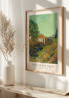 Aan een witte muur hangt een ingelijste poster van het landschapsschilderij van Vincent van Gogh uit 1883-1884, elegant weergegeven door middel van een magnetisch ophangsysteem. Onder het V. Van Gogh Weelderige Tuin Schilderij is "COLLAGEDEPOT" gedrukt, samen met "LANDSCHAP, 1883-1884." Op een tafel links staat een vaas met hoge gedroogde planten.,Lichtbruin