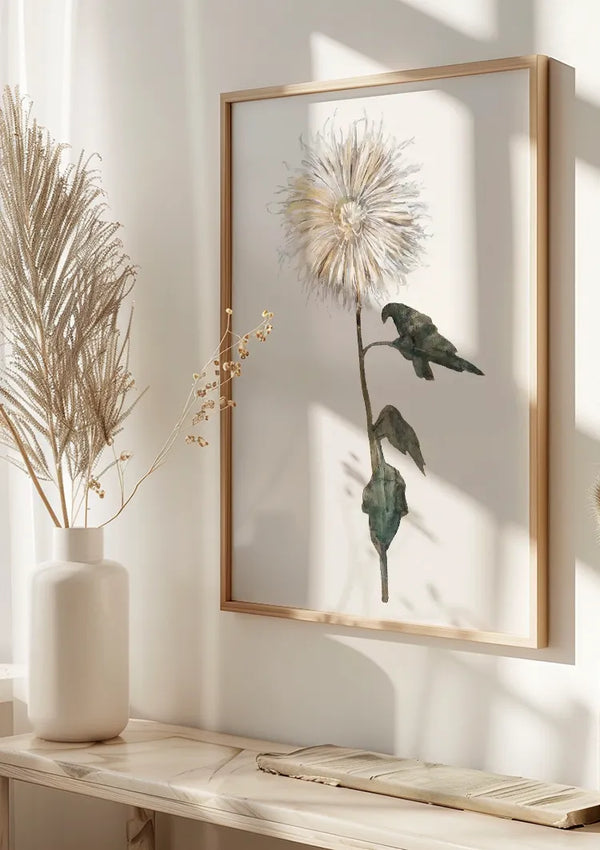 Aan een witte muur hangt een ingelijste botanische aquarelillustratie Van Een Bloem Schilderij van CollageDepot van een bloem met kleine, gevederde bloemblaadjes en twee groene bladeren. Ernaast staat een witte vaas met hoog, beige gedroogd gras op een lichte houten plank. Zonlicht werpt schaduwen op de muur, wat de serene wanddecoratie versterkt.,Lichtbruin