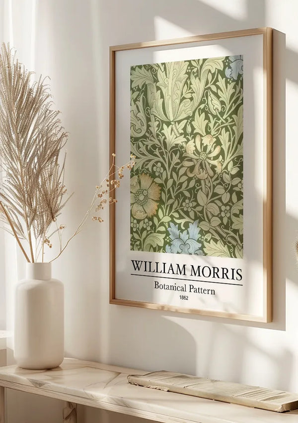 Aan de muur hangt een ingelijst botanische patroonschilderij van W. Morris, met een botanisch patroon van William Morris. De tekst op de poster luidt: "William Morris Botanical Pattern 1862." Gemonteerd door middel van een magnetisch ophangsysteem, zit een gedroogde plant in een witte vaas onder deze elegante wanddecoratie van CollageDepot.,Lichtbruin