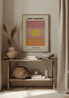 Een ingelijst CollageDepot A. Warhol - Sunset 1972 schilderij hangt aan een beige muur. Hieronder complementeert een houten plank met diverse neutraal getinte decoratieve items, waaronder manden, vazen en een gevouwen stof, het minimalistische kunstwerk wanddecoratie.,Lichtbruin