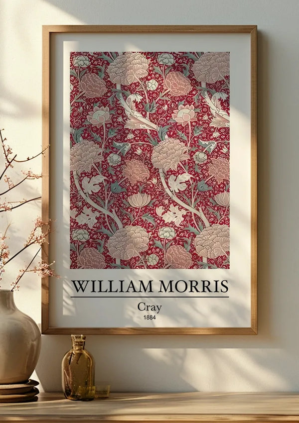 Een ingelijste poster toont een ontwerp van William Morris met de titel "Cray" uit 1884. Het prachtige CollageDepot W. Morris Cray Schilderij heeft roze en crèmekleurige bloemenpatronen op een rode achtergrond. Het frame staat op een houten plank naast een keramische vaas met een kleine tak met delicate knoppen, als aanvulling op de algehele wanddecoratie.,Lichtbruin