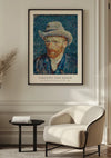 Een ingelijst *CollageDepot V. Van Gogh Zelfportret Met Grijze Vilten Hoed - 1887 Schilderij* hangt aan een beige muur. Onder het schilderij staat een moderne witte fauteuil en een klein zwart bijzettafeltje met boeken, gelegen in een goed verlichte kamer met een minimalistisch design.,Zwart
