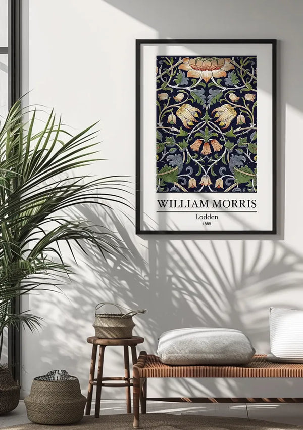 Ingelijste poster van een ontwerp van William Morris met de titel "W. Morris Lodden Schilderij" op een witte muur. Beneden staat een bank met een bruin kussen en een wit kussen, naast twee manden. Aan de linkerkant staat een hoge plant en zonlicht werpt schaduwen op de vloer en de muur, wat de boeiende wanddecoratie van CollageDepot versterkt.,Zwart