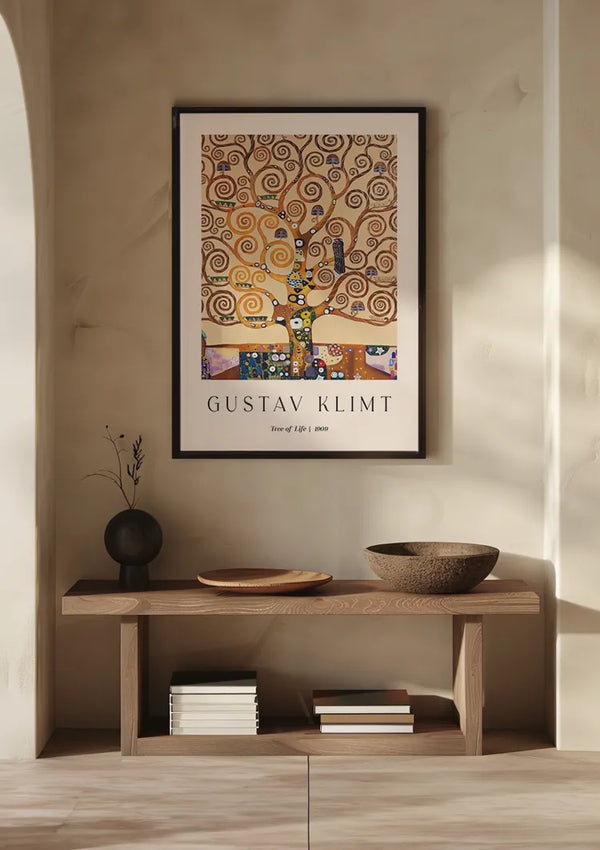 Een **CollageDepot Gustav Klimt Tree Of Life Schilderij** hangt aan een beige muur als boeiende wanddecoratie boven een houten consoletafel. Op de tafel staat een vaas met gedroogde bloemen, twee gestapelde boeken en twee houten schalen. Zacht natuurlijk licht verlicht de scène.,Zwart