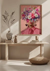 Een ingelijst kunstwerk, getiteld "Pink Flower Lady Schilderij" van CollageDepot, toont het gezicht van een vrouw verduisterd door een arrangement van kleurrijke bloemen en wordt getoond als een opvallende wanddecoratie op een houten consoletafel. Op de tafel staan ook een witte vaas, een grijze vaas met takken en een kleine beige urn. Ervoor ligt een kussen op de grond.,Lichtbruin