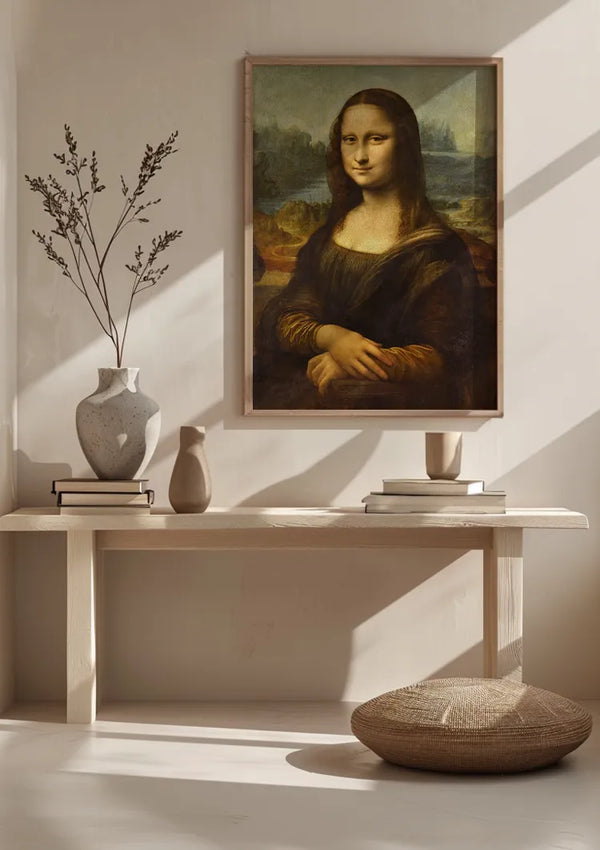 Een minimalistische kamer heeft een ingelijste print van het Iconische Portret Van Mona Lisa Schilderij van CollageDepot aan de muur, elegant opgehangen met een magnetisch ophangsysteem. Daaronder staat een houten tafel met twee vazen, enkele boeken en een klein beeldhouwwerk. Voor de tafel ligt een rond vloerkussen. Zonlicht werpt lange schaduwen door de kamer.,Lichtbruin