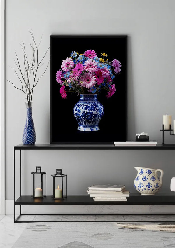 Een ingelijste foto van roze en gele bloemen in een blauw-witte vaas, het Delfts Blauw Bonte Bloemenpracht In Vaas Schilderij van CollageDepot, hangt aan een grijze muur, verhoogd door een magnetisch ophangsysteem. Daaronder staat op een zwarte plank een keramische vaas, twee zwarte lantaarns en enkele kaarsen. Links staat op de plank nog een blauw-witte vaas met dunne takken.,Zwart