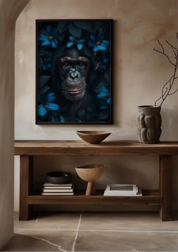 Een ingelijst Chimp And Butterflies Schilderij van CollageDepot van een chimpansee omringd door blauwe bloemen hangt aan een beige muur, gebruikmakend van een magnetisch ophangsysteem. Daaronder staat een houten consoletafel met twee houten schalen, een vaas en een stapel boeken. De kamer is voorzien van natuurlijke decorelementen en ademt een rustige sfeer uit.,Zwart