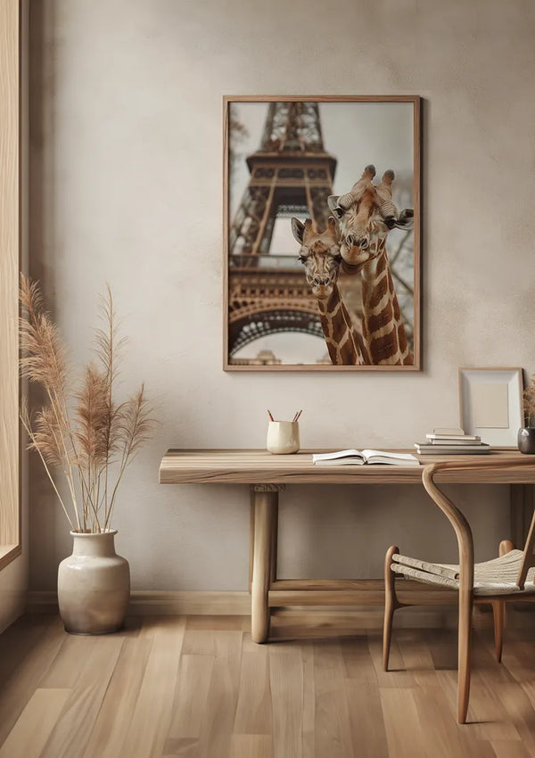 Een minimalistische kamer met een houten bureau met een gebogen stoel, een pot met decoratief gras en een foto aan de muur. Het kunstwerk toont twee giraffen met de Eiffeltoren op de achtergrond. De kamer bevat ook een beker met pennen en een open boek. Het lijkt erop dat de aaa 113 Exclusive van CollageDepot ontbreekt in uw bericht; Geef het op voor SEO-trefwoordidentificatie.,Lichtbruin