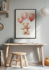 Een kinderkamer met een houten bureau en bijpassende kruk. Boven het bureau hangt een CollageDepot: een ingelijst Teddybeer Met Roze Ballonnetjes Schilderij. De muur is lichtgrijs en aan het plafond hangt een ronde papieren lantaarn. Sommige boeken en decorartikelen staan op de planken.,Zwart