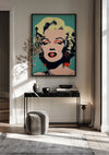 Een moderne woonkamer is voorzien van een groot CollageDepot Marilyn Monroe Karakteristiek Popart Portret Schilderij met blond haar en rode lippenstift aan de muur. Hieronder staat een zwarte consoletafel met decoratieve items, een grijze kruk met kussens en beige gordijnen naast een raam dat natuurlijk licht binnenlaat.